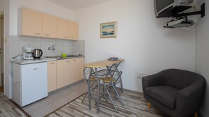 A compact kitchen with a dining area, a small TV, and a grey armchair. - Studio Paula 5 300m From Sea (Crikvenica)