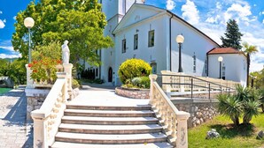 A white church with a clock tower, a stone staircase leading to the entrance, and a well-maintained garden. - Studio Paula 5 300m From Sea (Crikvenica)