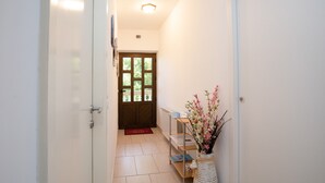 A hallway with a wooden door, a radiator, a shelf with books, and a vase with flowers. - Studio Paula 2 300m From Sea (Crikvenica)