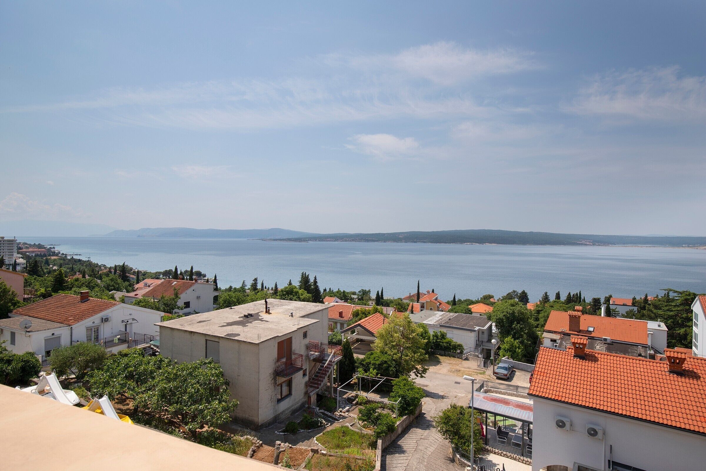 A coastal residential area with houses, a clear view of the sea, and distant mountains.