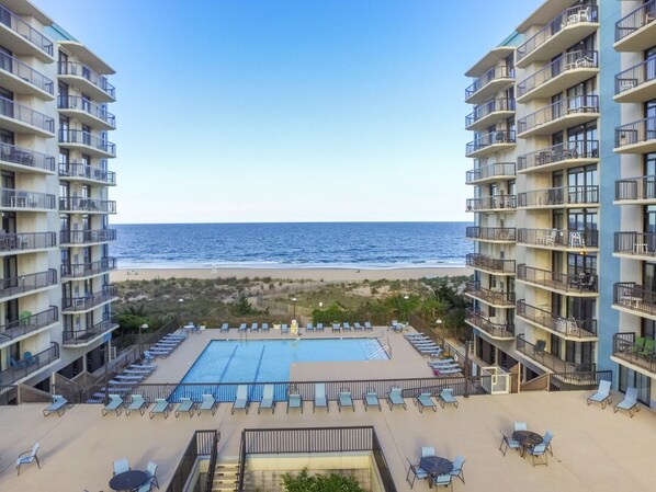 A hotel with a pool, lounge chairs, and a view of the beach and ocean.