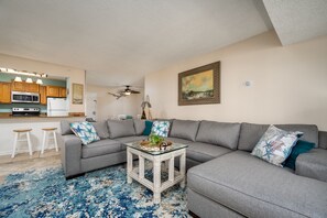 A modern living room with a gray sectional sofa, a glass coffee table, and a blue patterned rug.