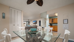 A dining area with a glass table and white chairs, a kitchen in the background, and a ceiling fan. - 2 Bedroom, 2 Bath Side Unit with fantastic views of the ocean and pool (Ocean City)