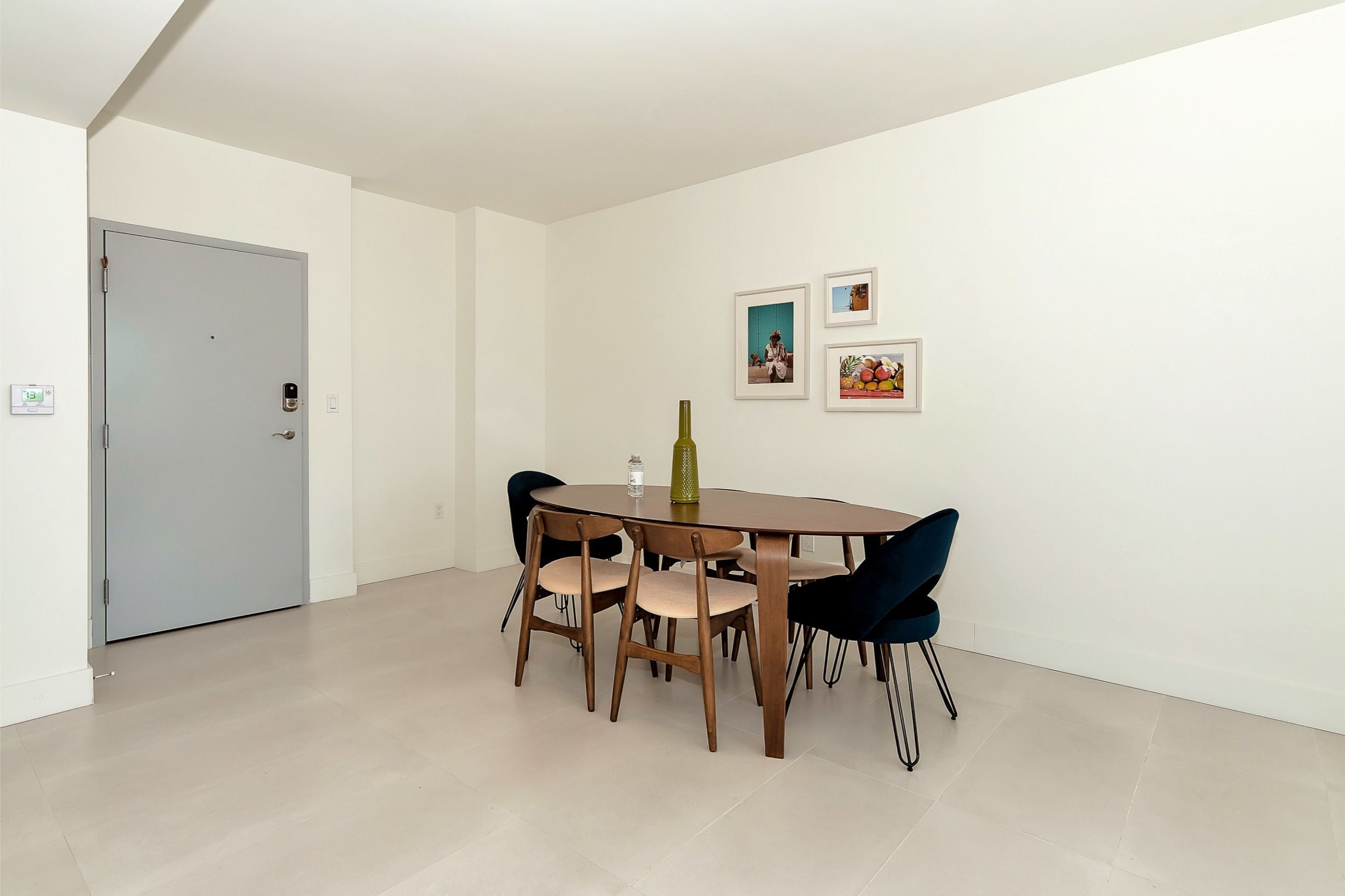 A dining area with a round table, four chairs, and a bottle of water. There are two framed pictures on the wall.