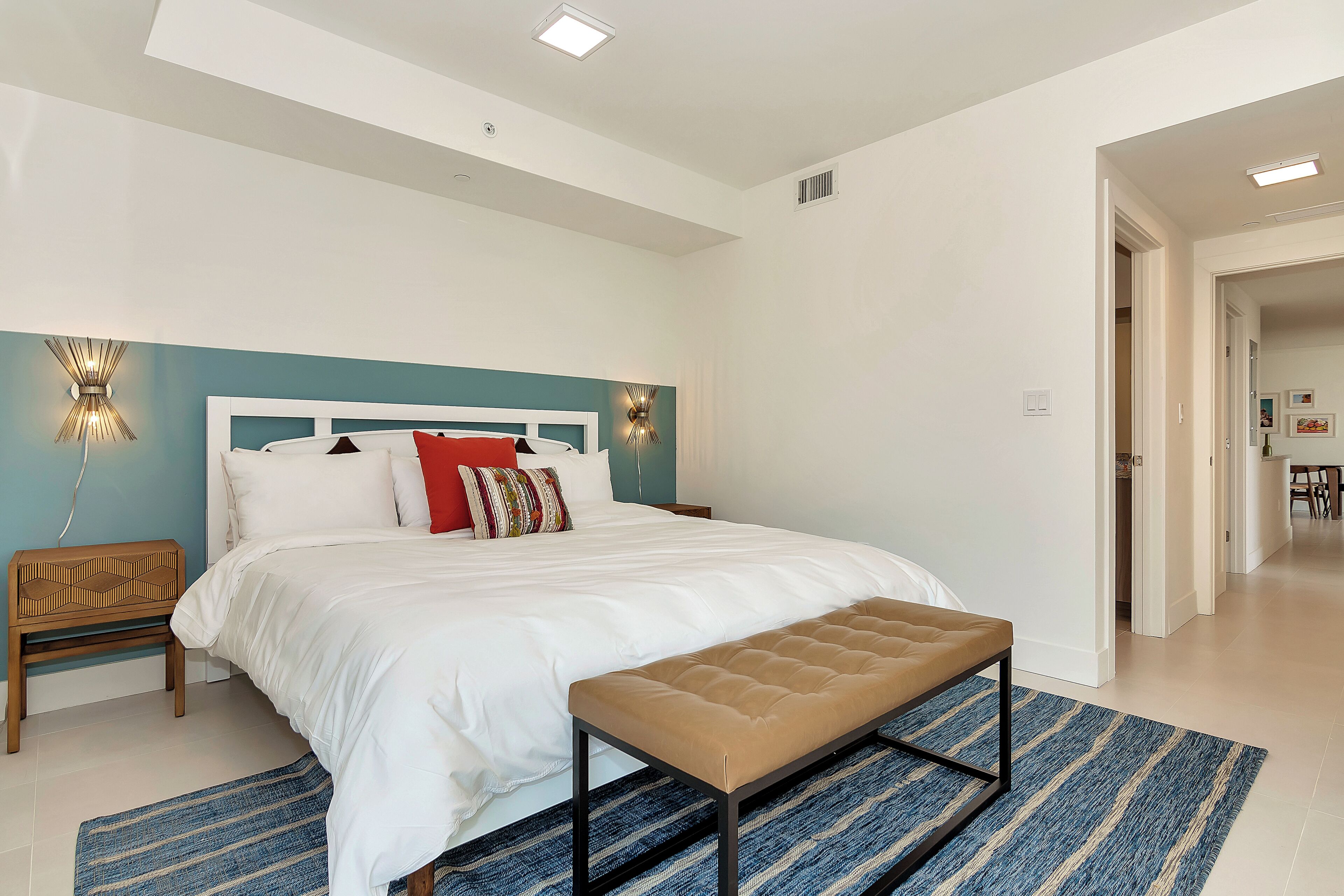 A modern bedroom with a large bed, a bench, and a blue striped rug.