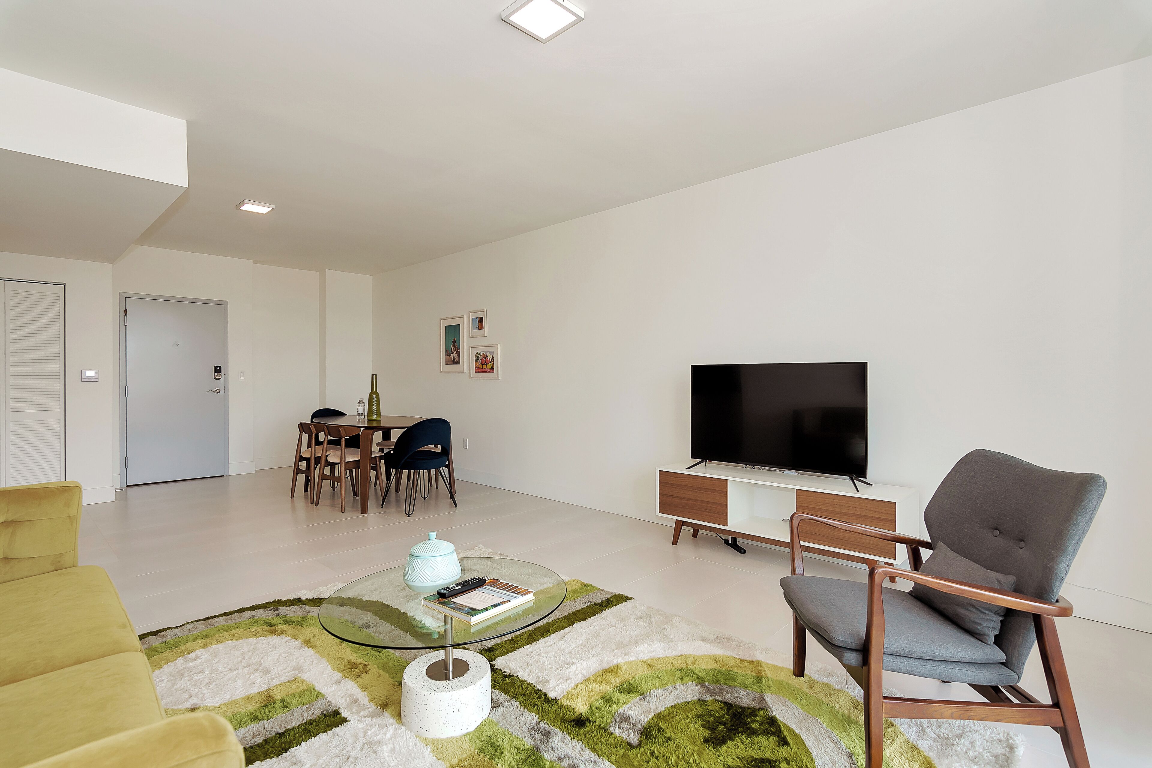 En moderne stue med sofa, sofabord i glas, fjernsyn og spiseplads med stole og bord.