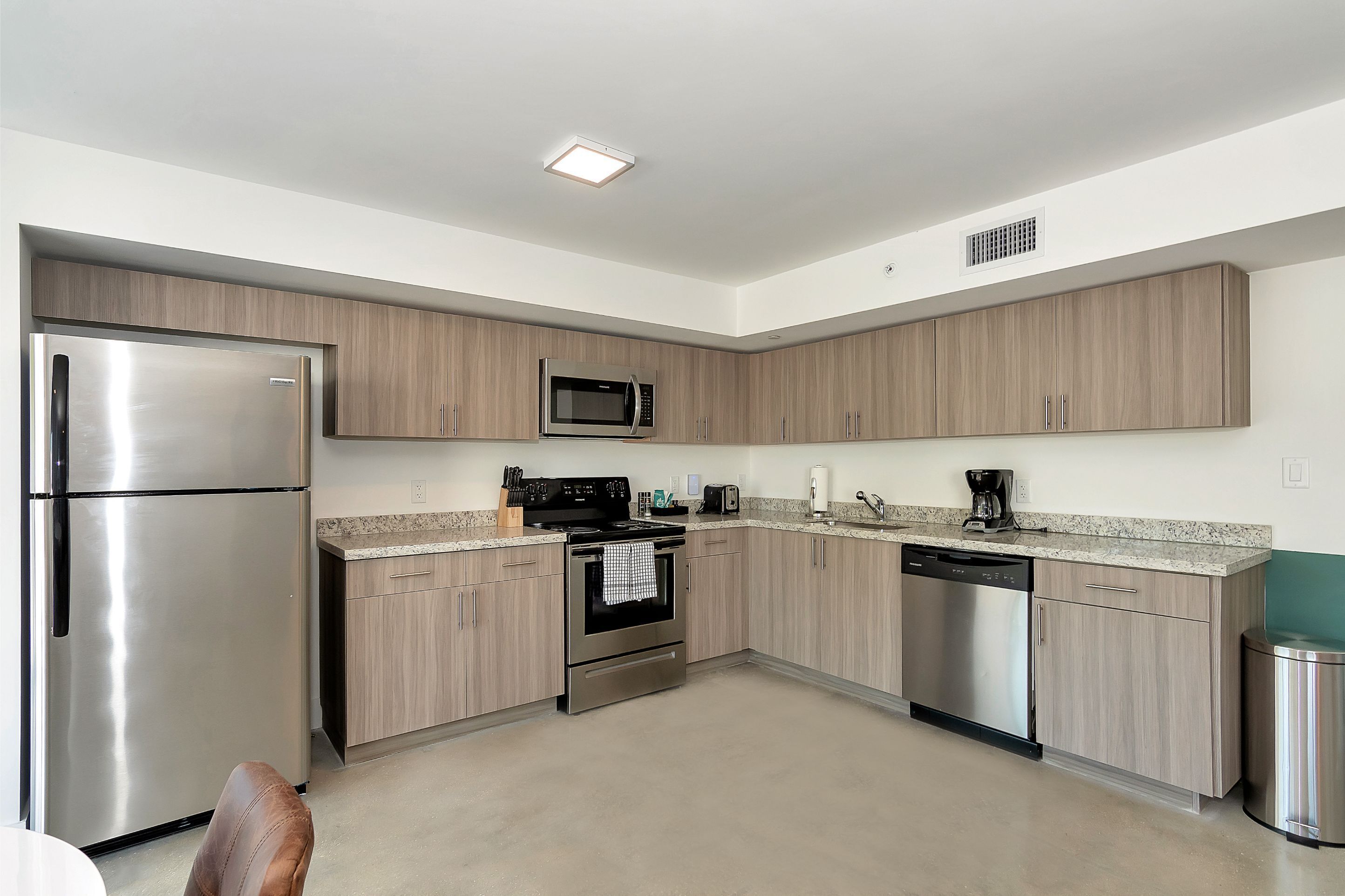 A modern kitchen with stainless steel appliances, light wood cabinets, and a granite countertop.