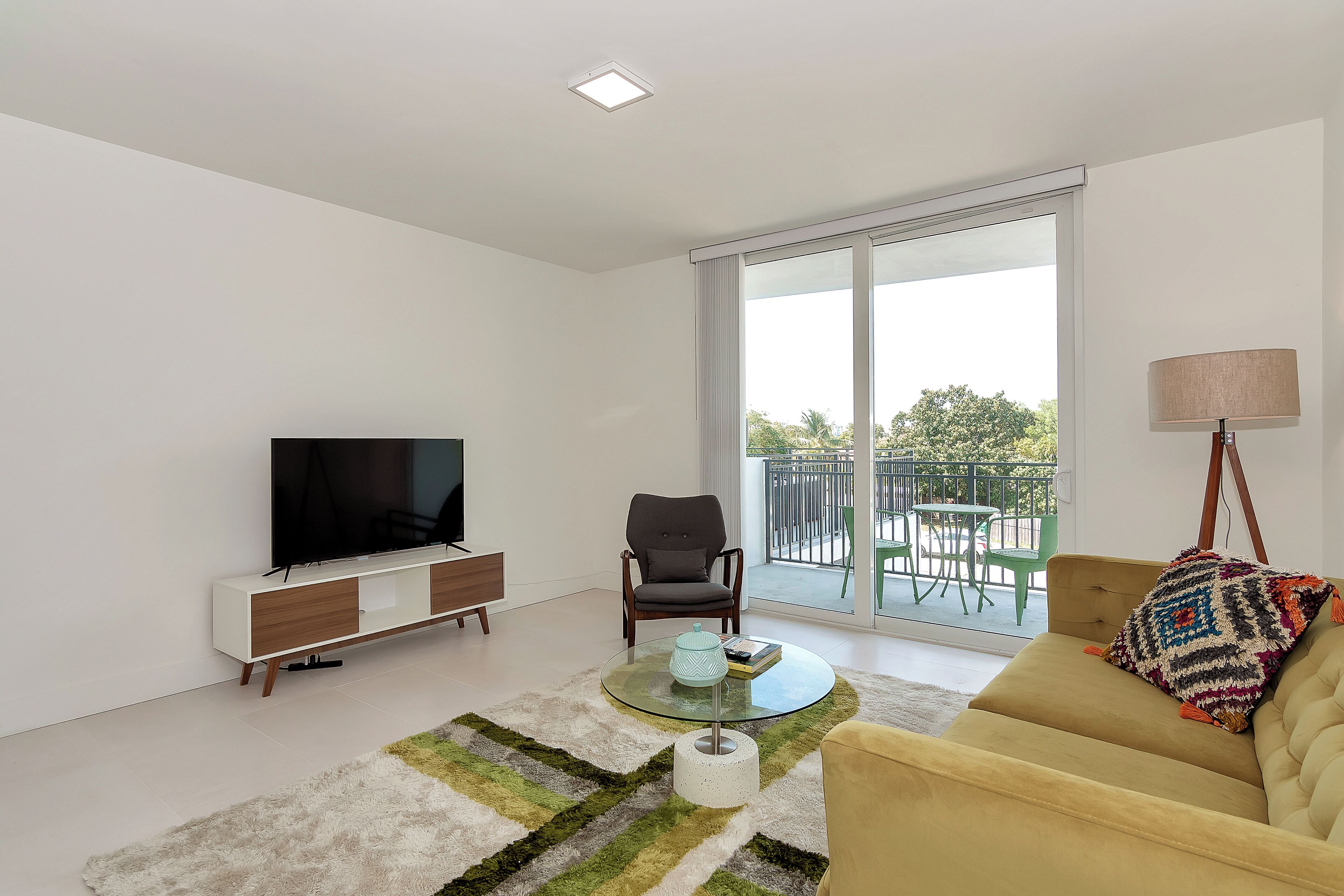 A modern living room with a flat-screen TV, a sofa, a chair, a coffee table, and a balcony with outdoor furniture.