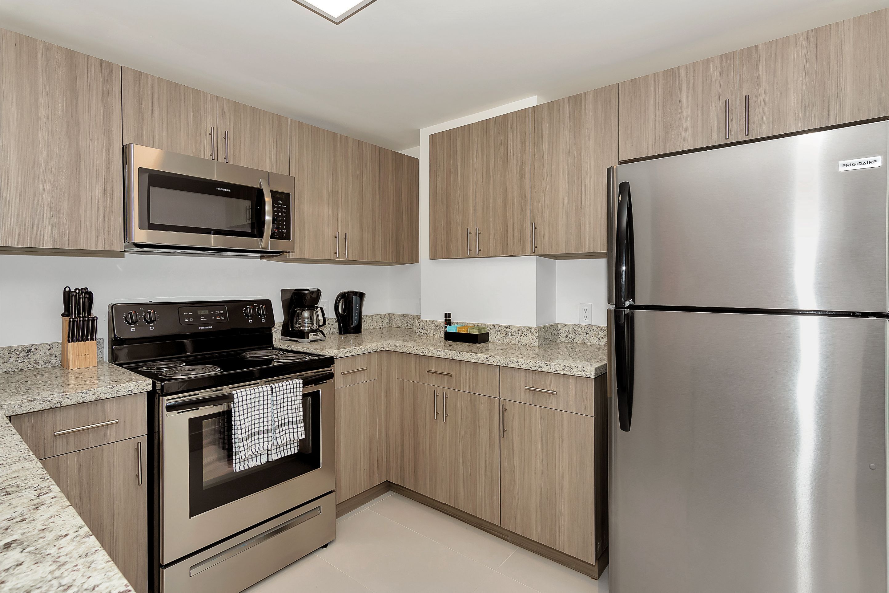 A modern kitchen with stainless steel appliances, light wood cabinetry, and a granite countertop.