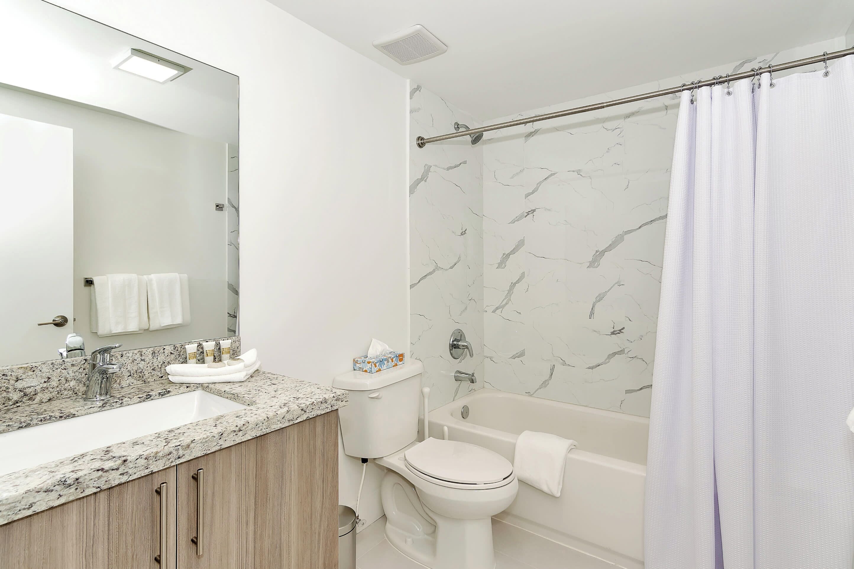 A bathroom with a marble backsplash, a sink, a toilet, and a bathtub.