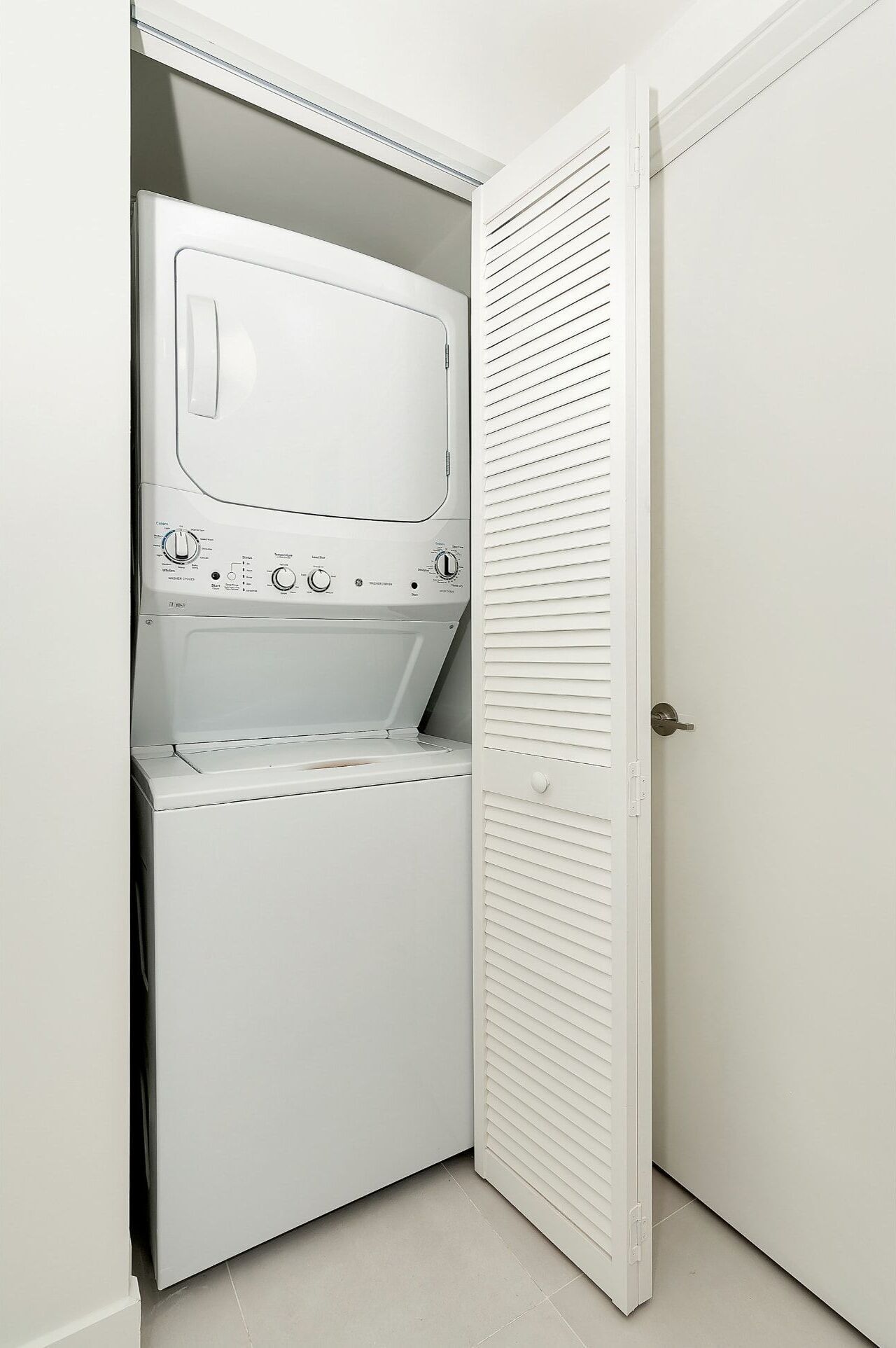 A laundry room with a washer and dryer, a door with louvered panels, and a tiled floor.