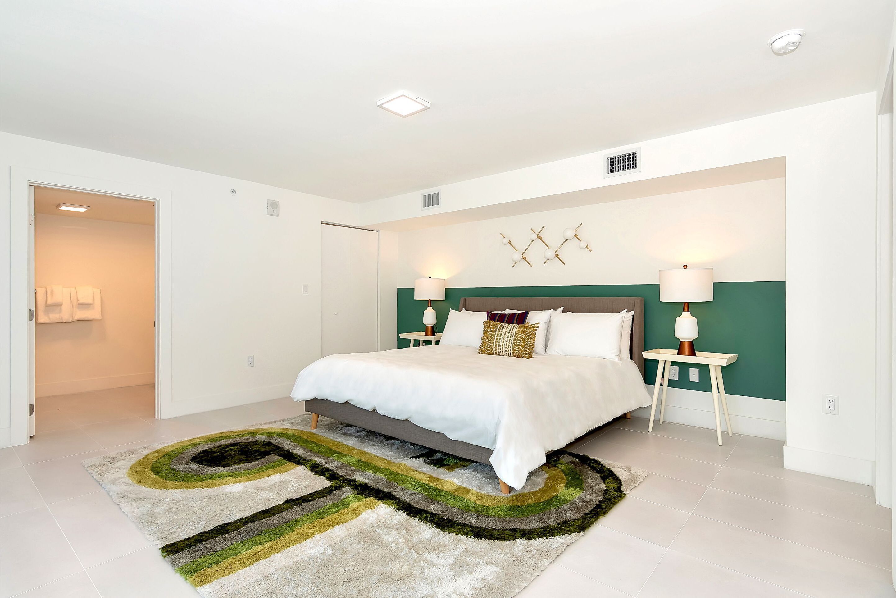 A modern bedroom with a bed, bedside lamps, and a decorative wall piece.