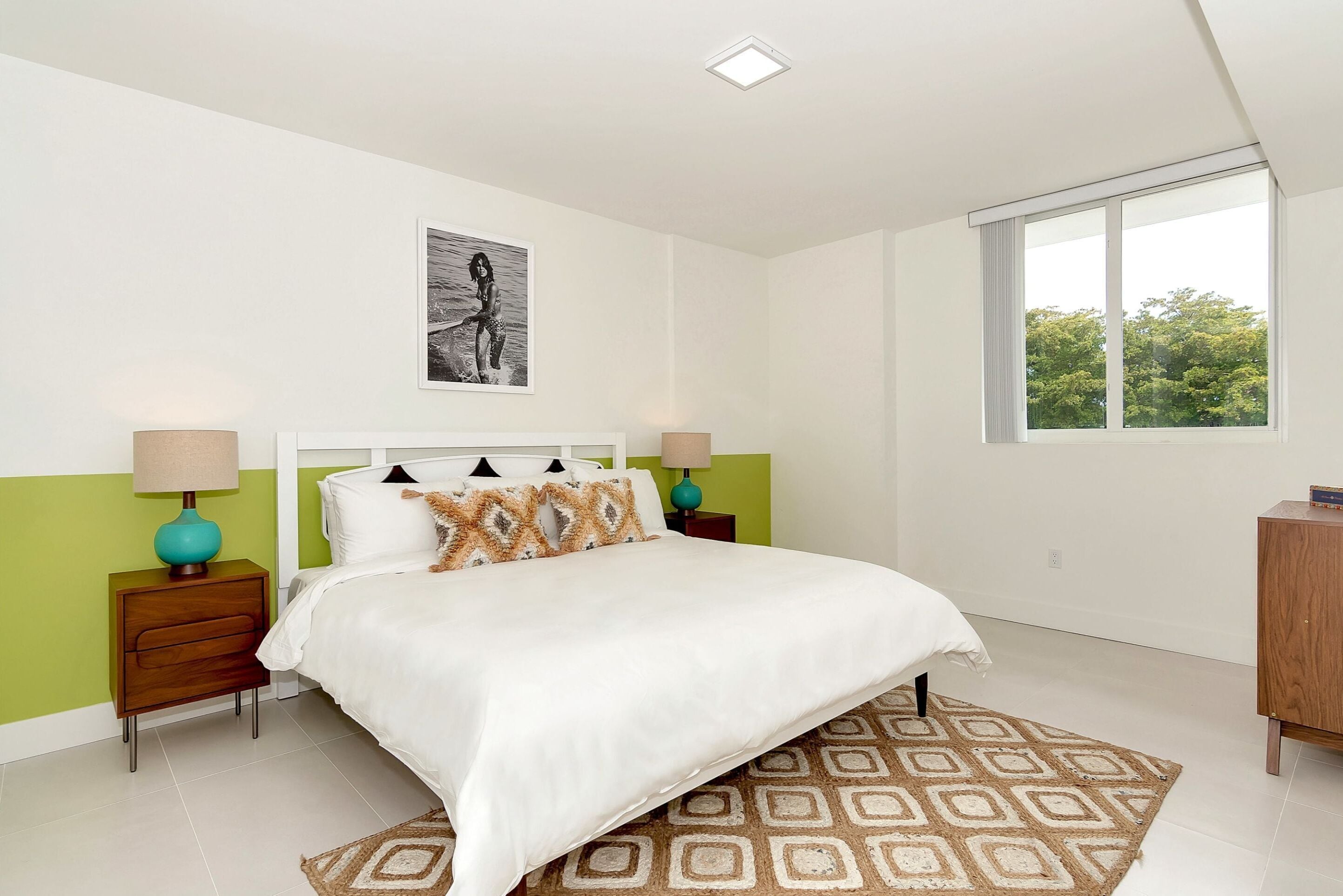 A bedroom with a bed, two nightstands, a window, and a painting on the wall.