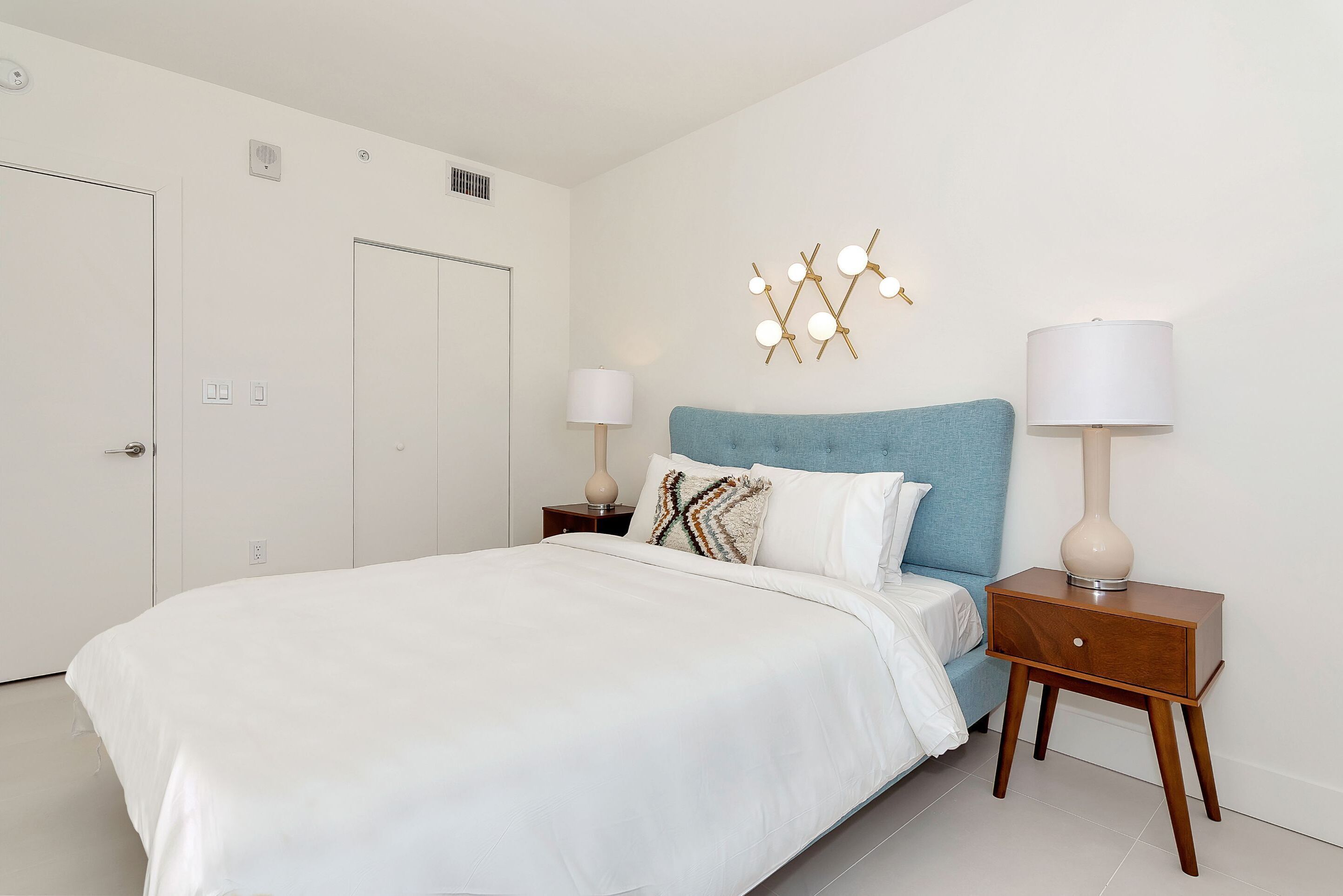 Une chambre à coucher avec un lit, une table de chevet avec une lampe, un luminaire fixé au mur et une porte.