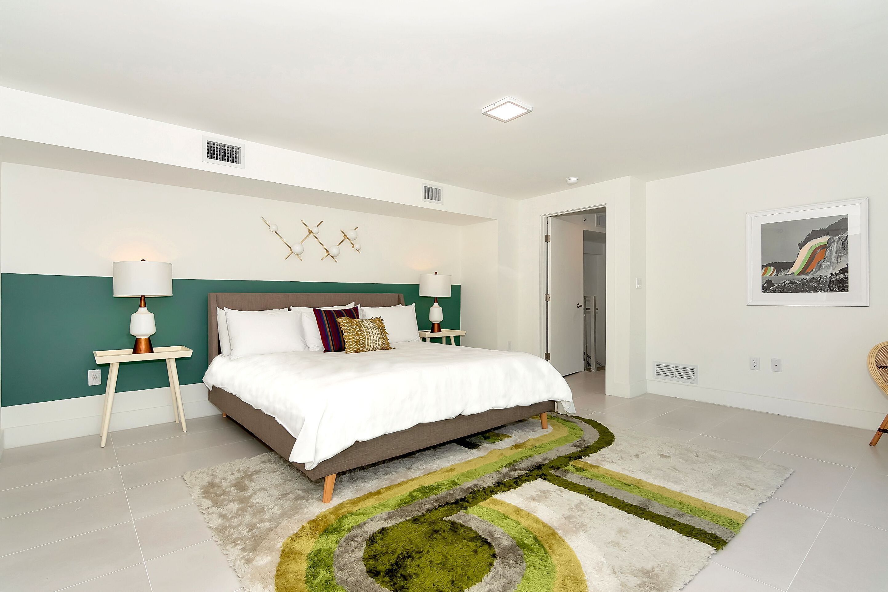 A bedroom with a bed, nightstands, a lamp, a rug, and a wall art piece.