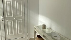 A hallway with a white door, a glass-top console table with baskets, and wall-mounted lighting.