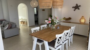 A dining area with a wooden table, white chairs, a vase of flowers, and wicker pendant lights.