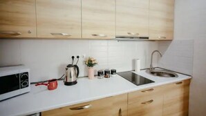 Una cucina con mobili in legno, un piano di lavoro bianco, un lavandino in acciaio inossidabile, un bollitore, una tazza rossa e un forno a microonde.