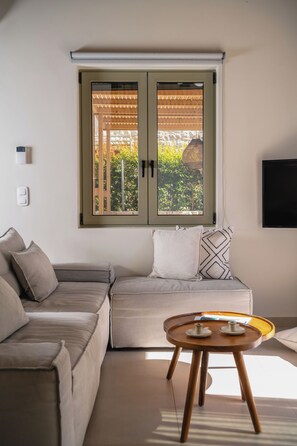 A modern living room with a sectional sofa, a small wooden table, and a large window with a wooden pergola.