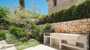 Zona cuina a l'aire lliure amb mur de pedra, una barbacoa i un rentaplat.