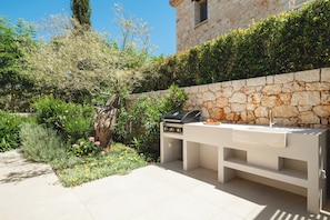 An outdoor kitchen area with a stone wall, a grill, and a sink.