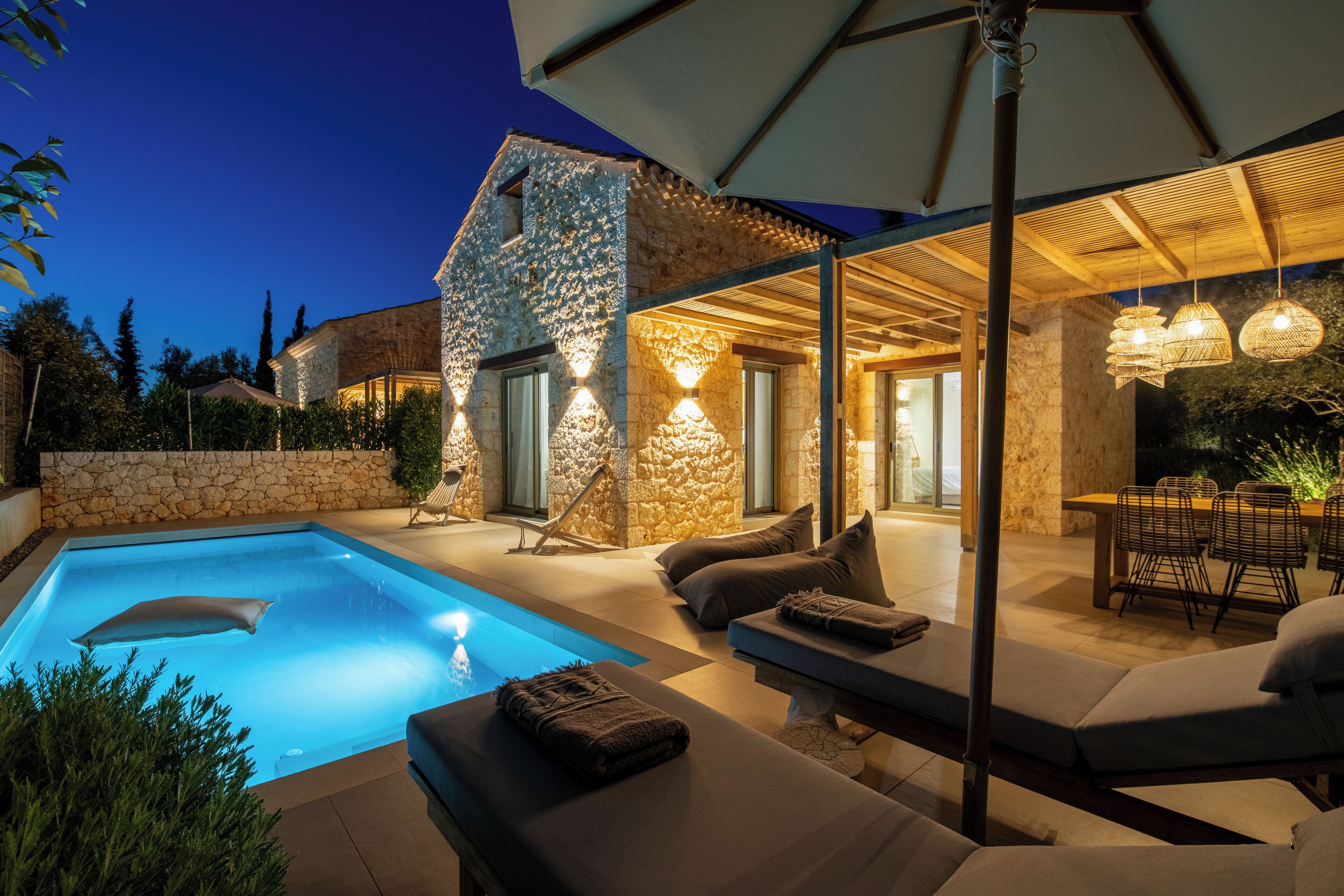 A modern outdoor pool area with stone walls, lounge seating, and ambient lighting.