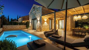 A modern outdoor pool area with stone walls, lounge seating, and ambient lighting.