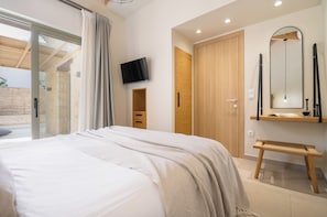 A modern bedroom with a large bed, a television, a wooden wardrobe, and a bench.