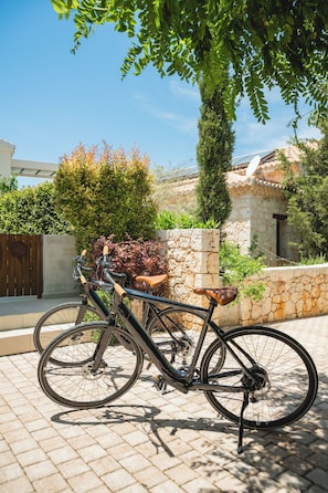 A bicycle parked on a paved surface with a stone wall and greenery in the background.