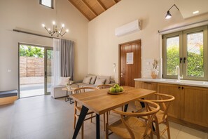 A modern kitchen with a wooden table and chairs, a built-in oven, and a large window with a view of greenery.