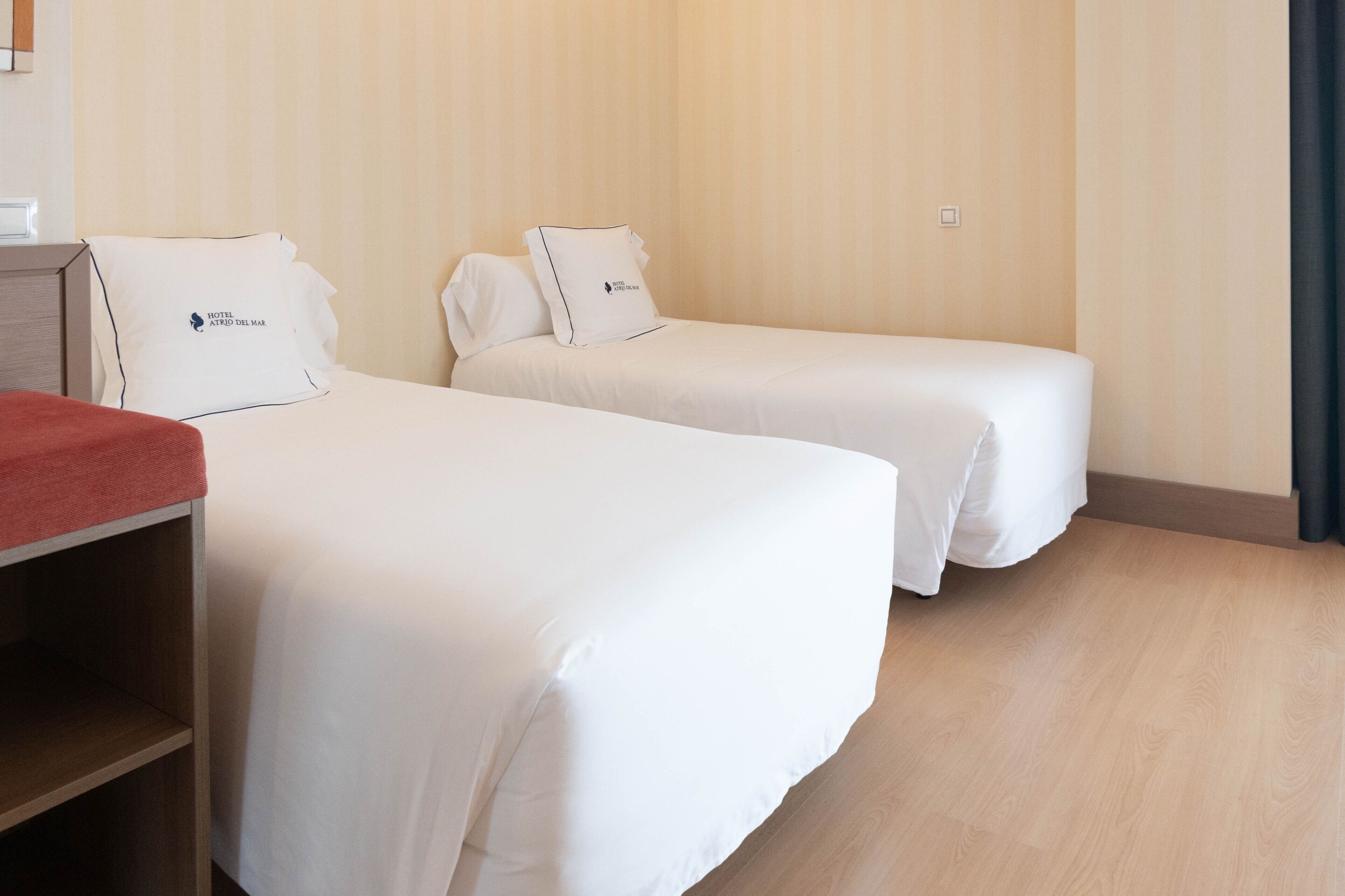 A hotel room with two single beds, a wooden nightstand, and a red throw blanket.
