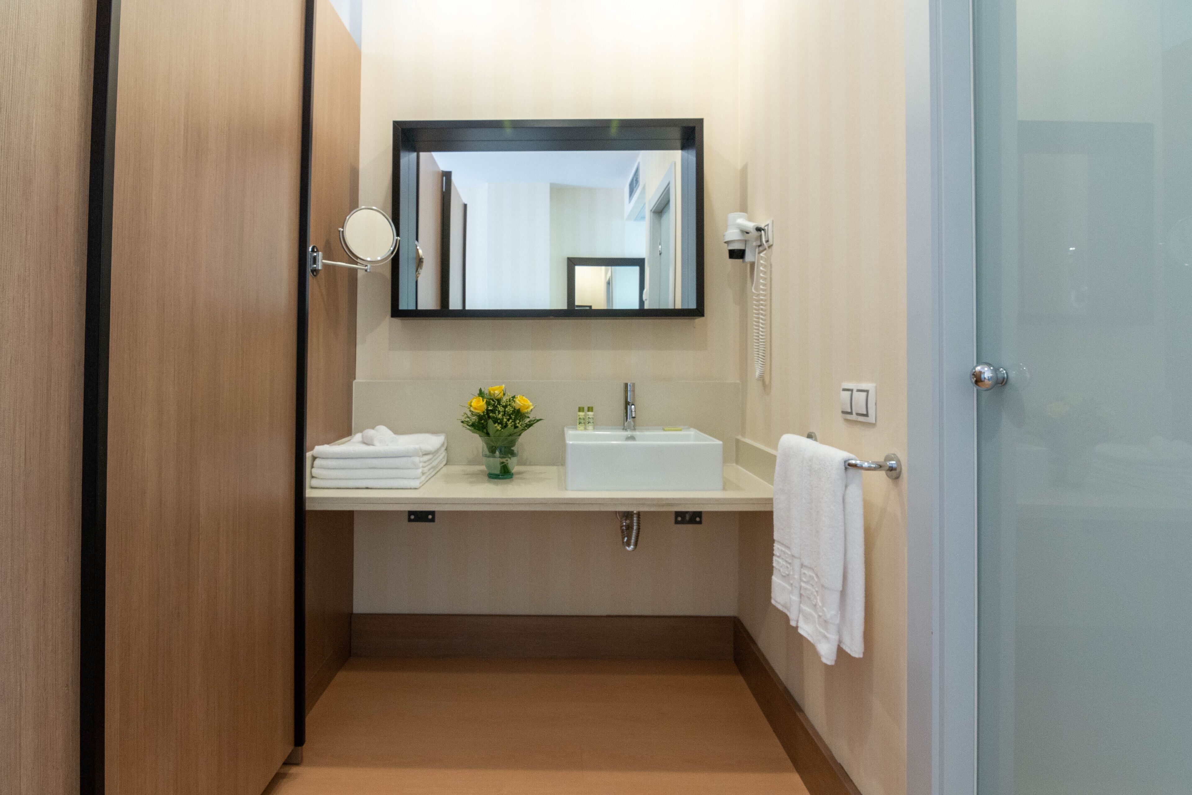 A compact bathroom with a wooden door, a white sink, a mirror, a hairdryer, and a towel rack.