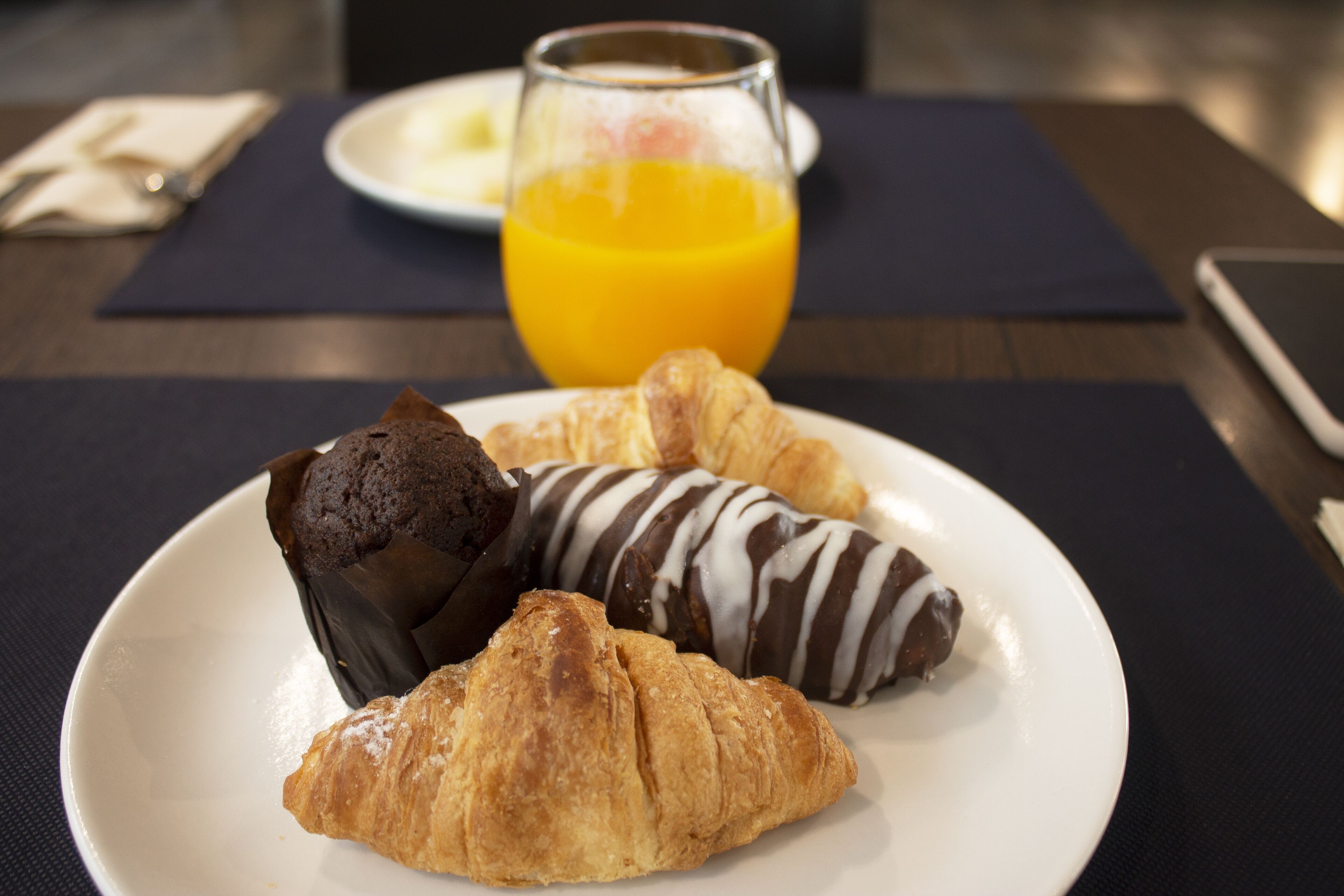 A breakfast plate with croissants and a muffin, a glass of orange juice, and a plate of eggs and toast.