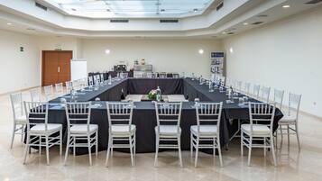 Un salón de conferencias con una larga mesa, sillas blancas y techo de cristal.