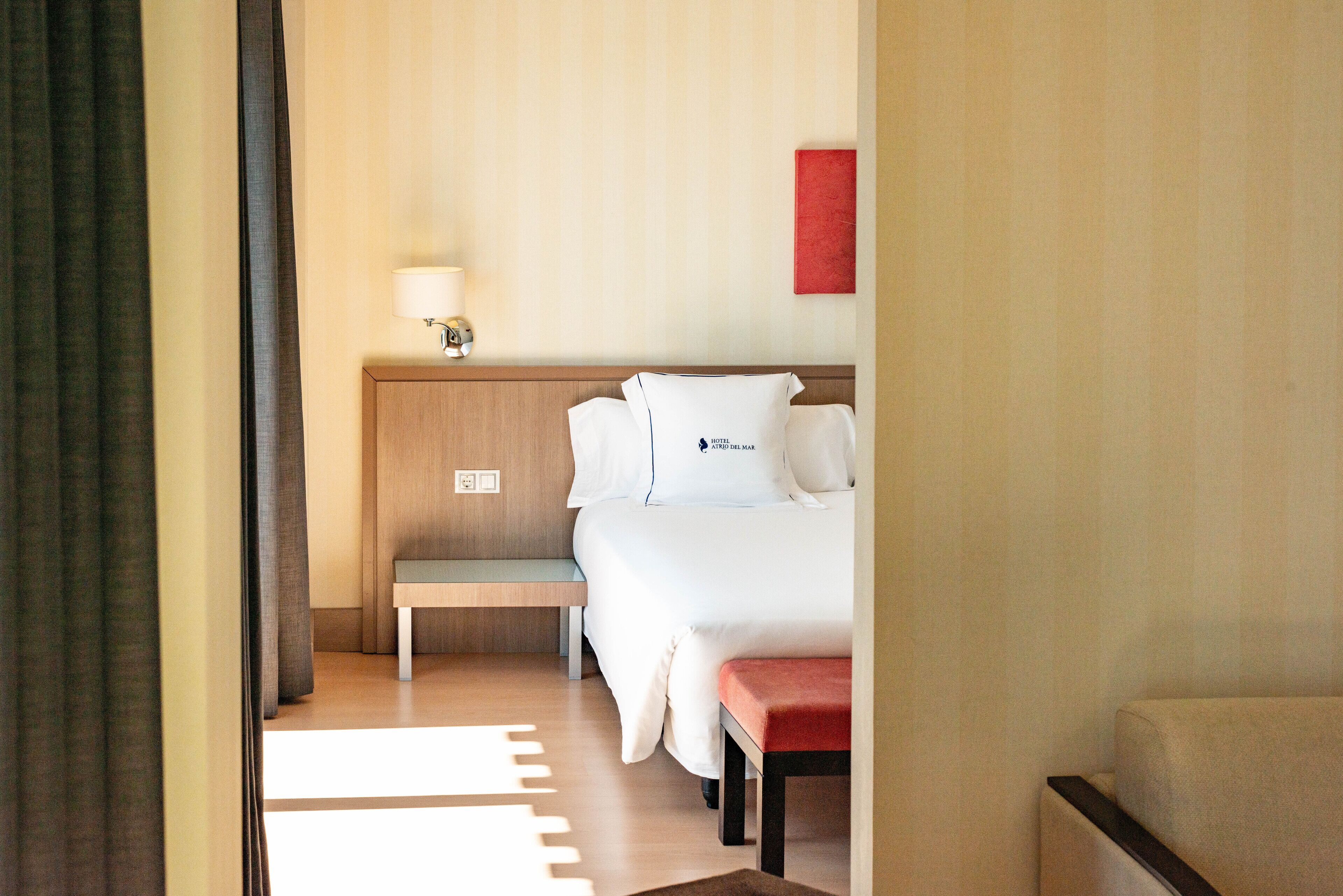 A hotel room with a bed, a bedside table, a lamp, and a red wall decoration.