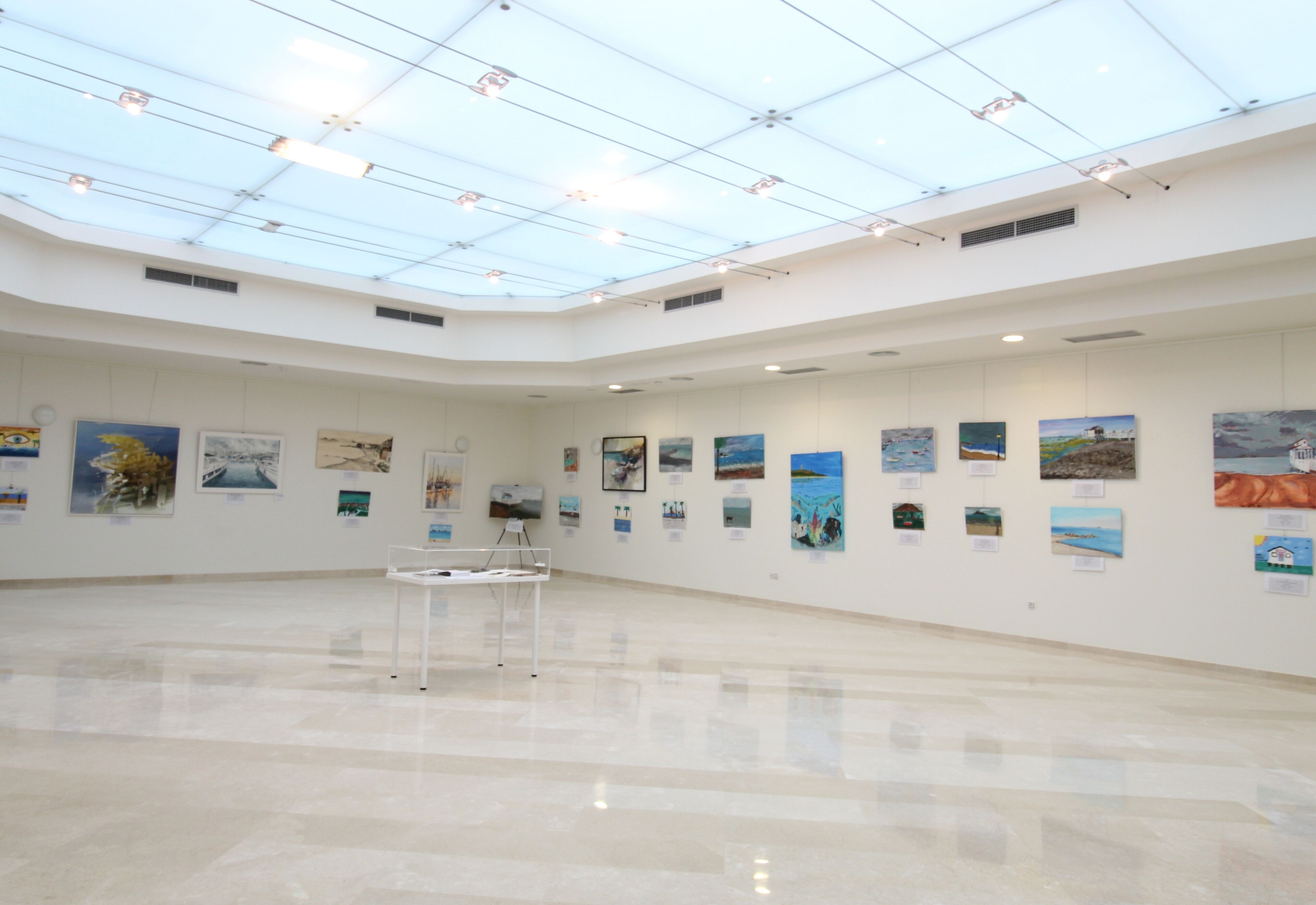 A spacious gallery with a high ceiling and skylight, displaying various artworks on the walls.