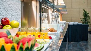 Een buffet met verschillende soorten fruit, vruchtensappen en gebak.