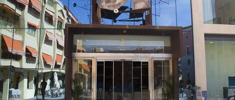 A hotel entrance with a glass facade, a modern design, and a visible outdoor seating area.