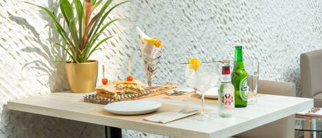 A dining table with a plant, a sandwich, a glass of water, and a bottle of beer.