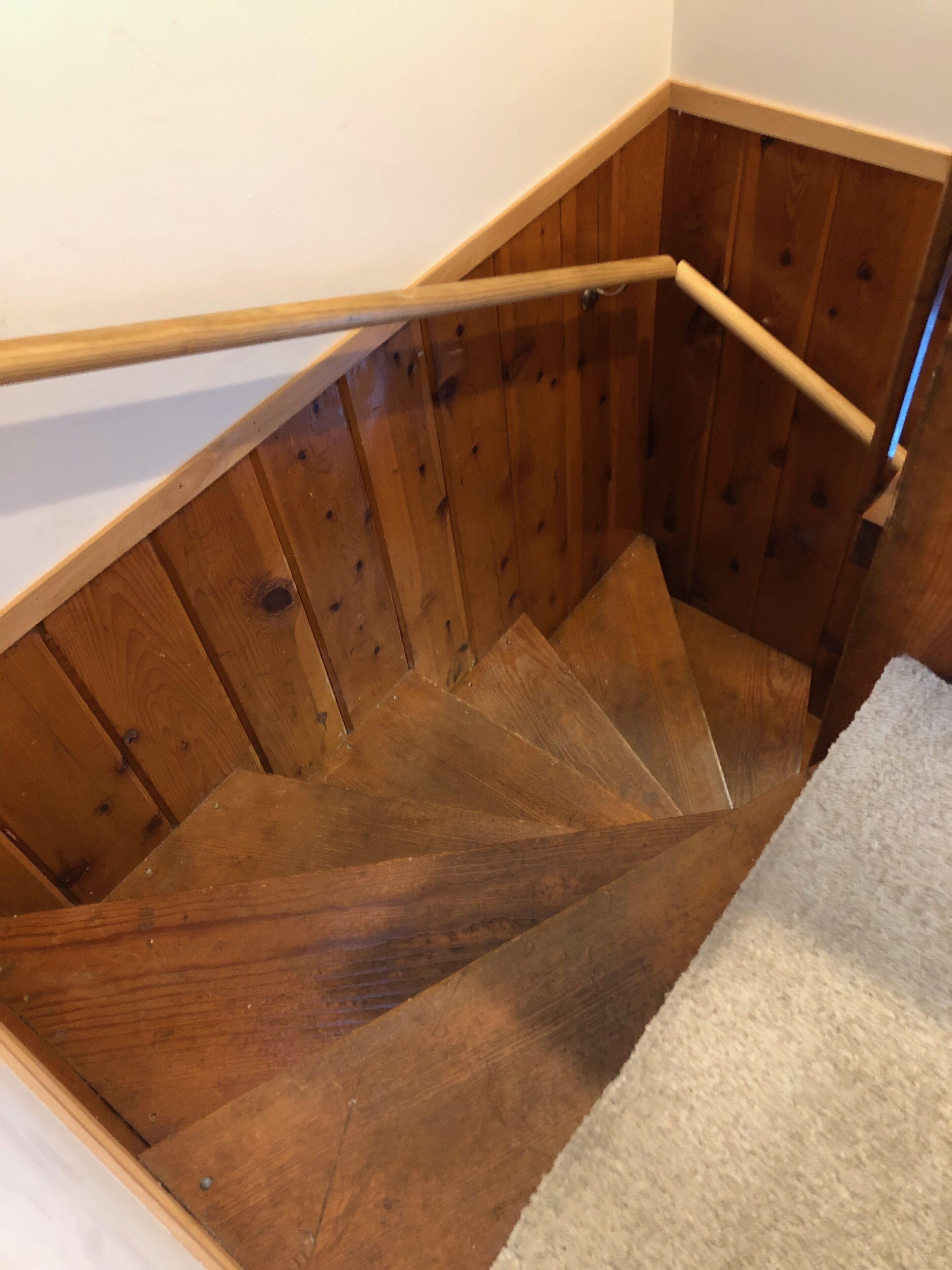 A wooden staircase with a handrail, carpeted landing, and wooden walls.