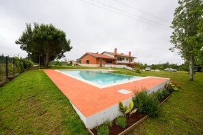 Uma casa com piscina, cercada por um gramado bem cuidado e árvores.