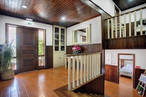 A hotel lobby with a wooden staircase, a reception desk, and a bed in the background.