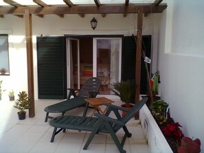 Een overdekt terras met twee loungestoelen, een bijzettafeltje en plantenpotten.