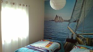 Quarto com duas camas, uma janela grande com cortinas, um mural de um veleiro na parede e um lustre.
