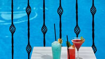 A poolside table with two drinks and a martini glass, set against a blue pool with decorative metal railings.