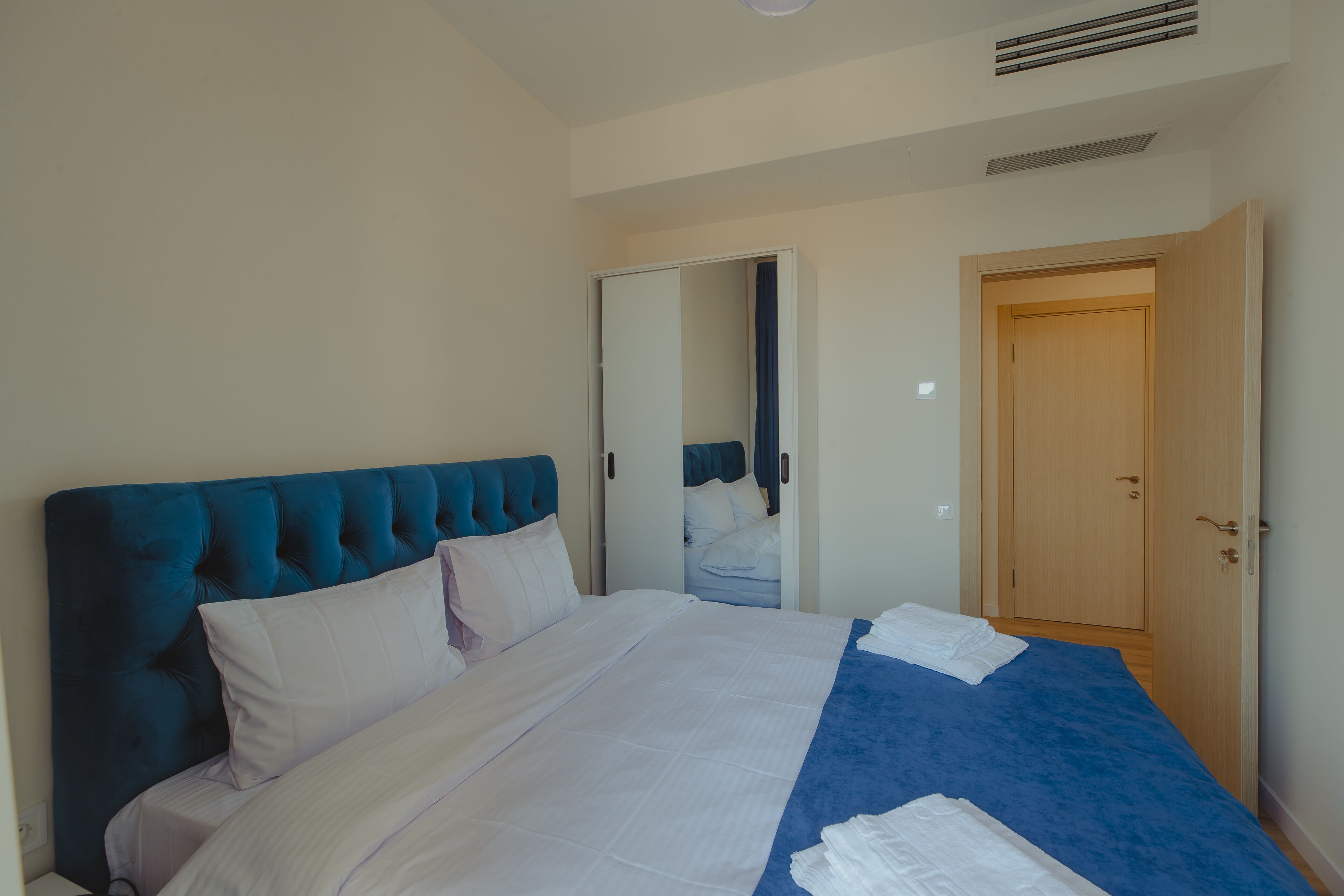 A bedroom with a large bed, a wooden wardrobe, and a door leading to another room.