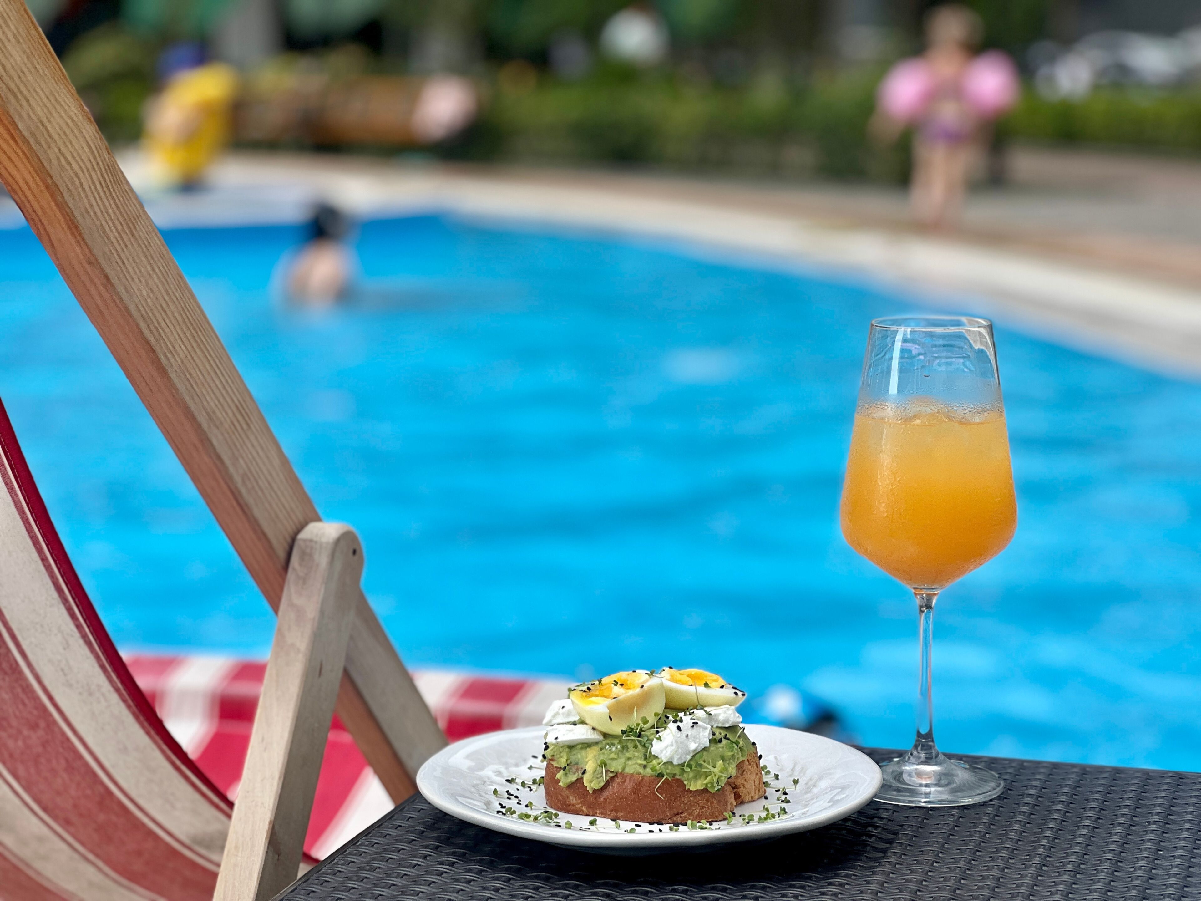 Un tavolo da pranzo con un piatto di cibo e un bicchiere di succo d'arancia vicino a una sedia a bordo piscina.