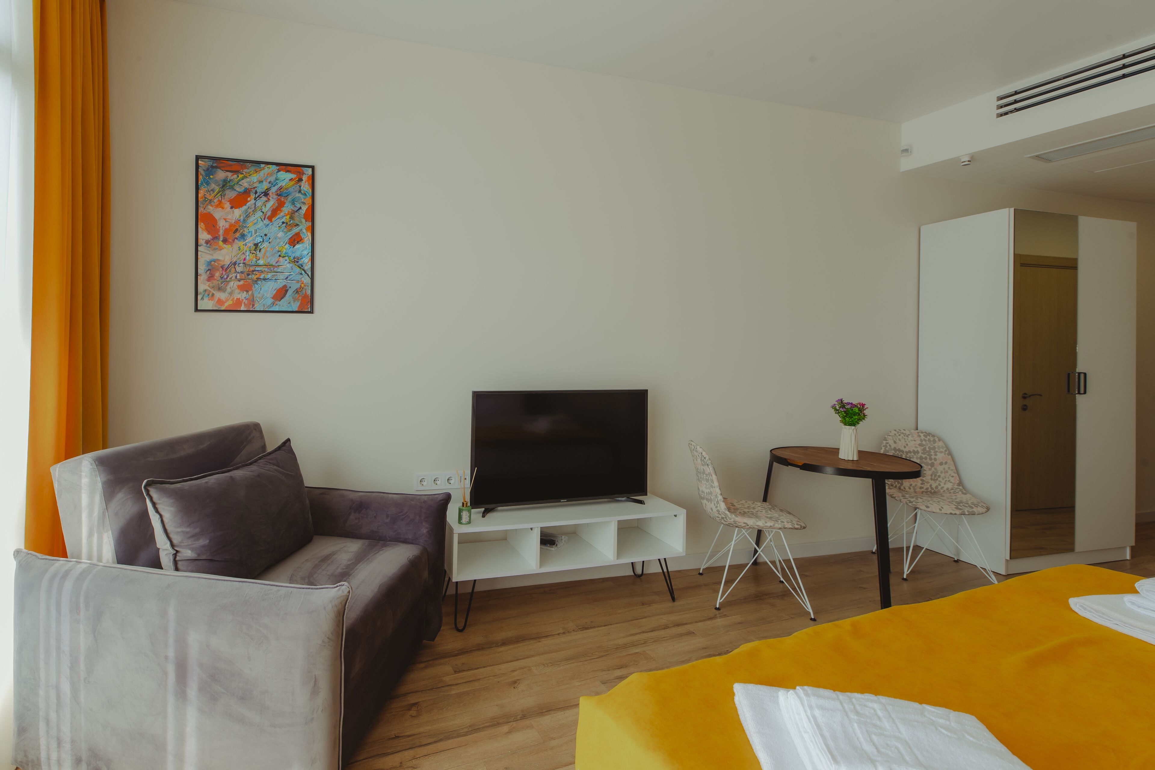 Una habitación de hotel con sofá, cama, televisión, una mesita con un florero y una silla.