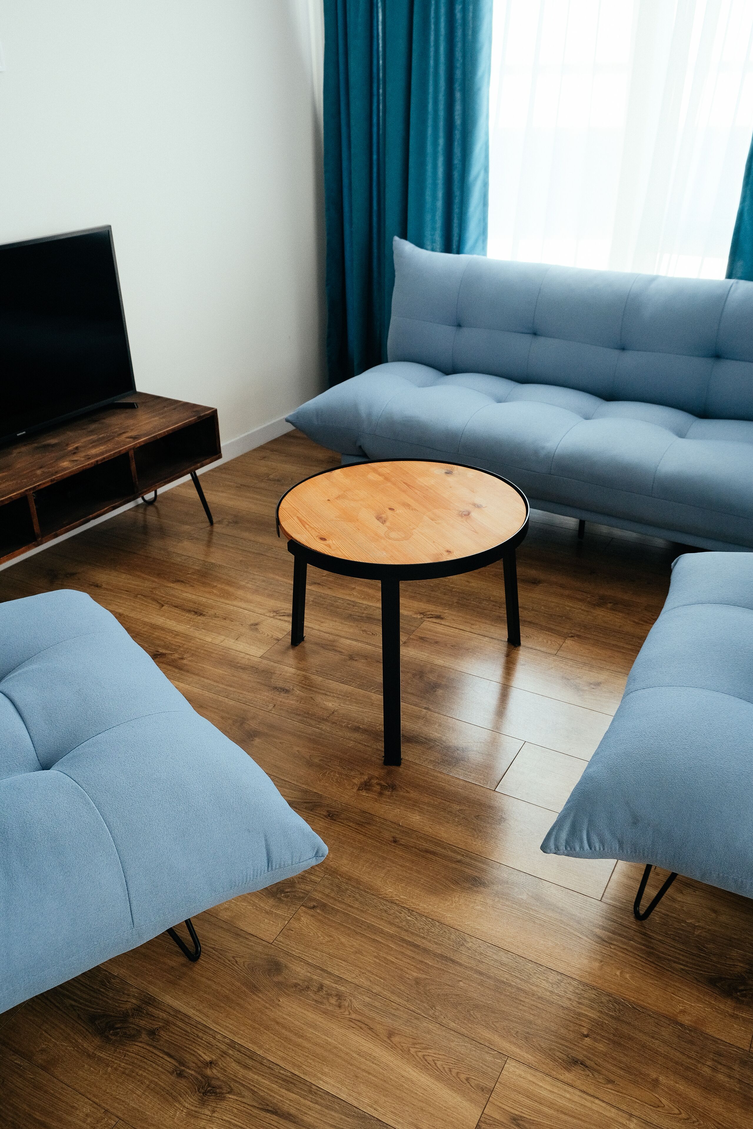Een moderne woonkamer met een houten salontafel, twee blauwe banken en een televisie op een houten dressoir.