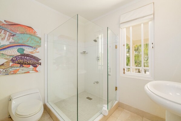 A bathroom with a glass-enclosed shower, a toilet, a sink, and a window with a view of greenery.